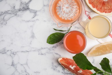 Glasses of different pomelo juices and fruits on white marble table, flat lay. Space for text