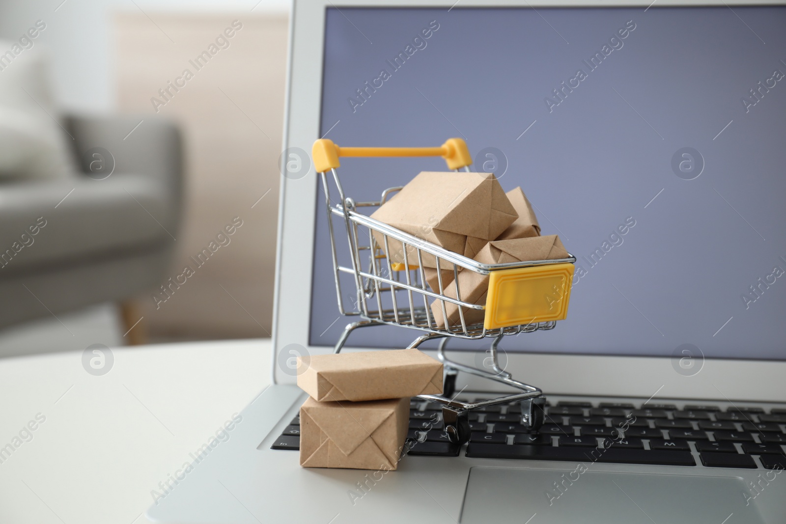 Photo of Internet shopping. Laptop and small cart with boxes on table indoors