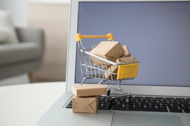 Internet shopping. Laptop and small cart with boxes on table indoors