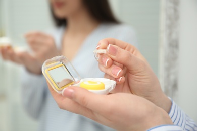 Photo of Young woman taking contact lens from container indoors