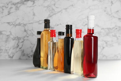 Bottles with different kinds of vinegar on table against marble background