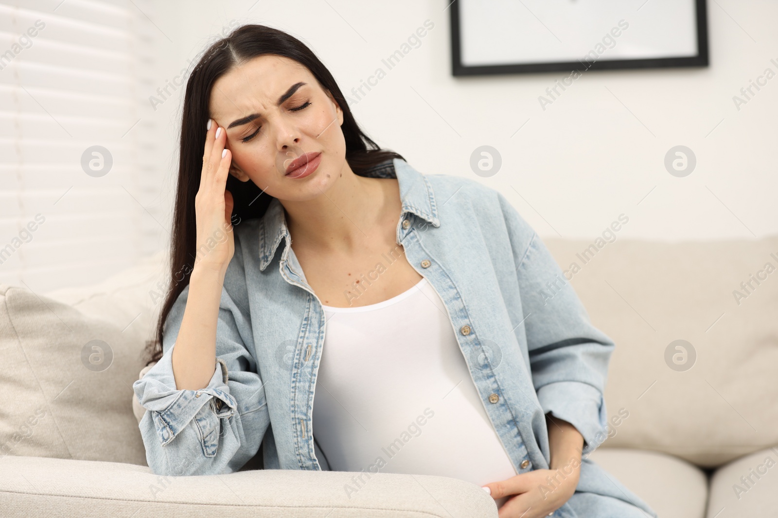 Photo of Pregnant woman suffering from headache on sofa at home