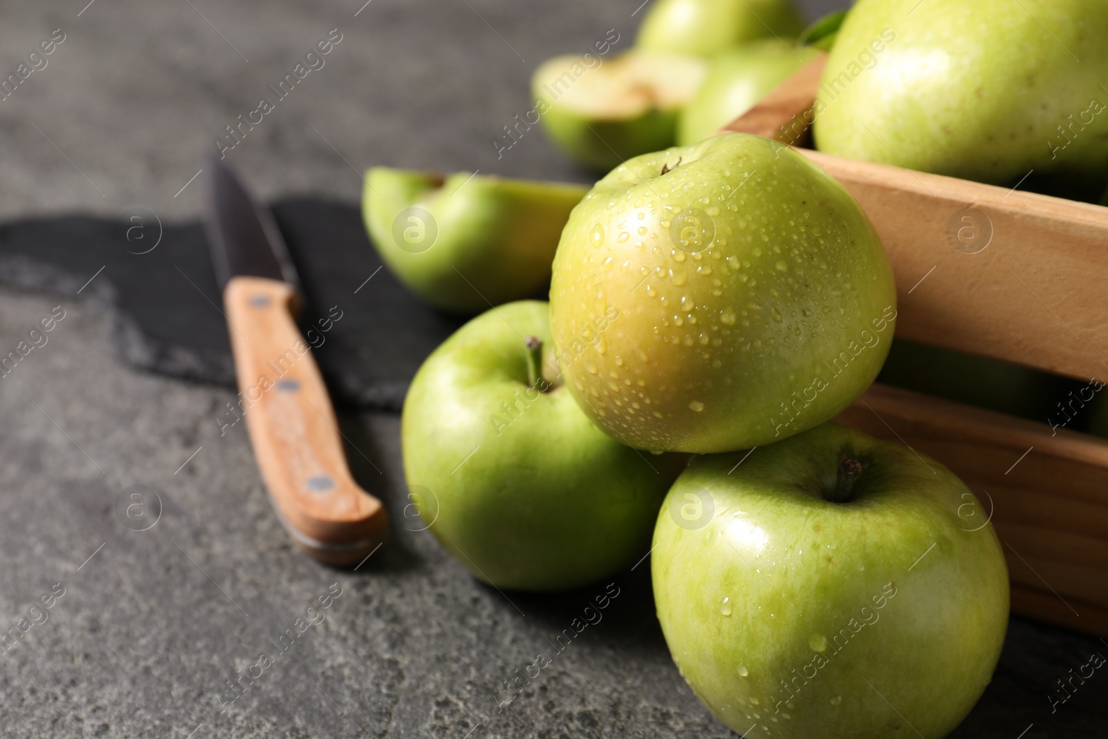 Photo of Ripe green apples with water drops and knife on grey table, closeup