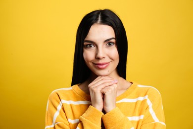 Portrait of happy young woman with beautiful black hair and charming smile on yellow background