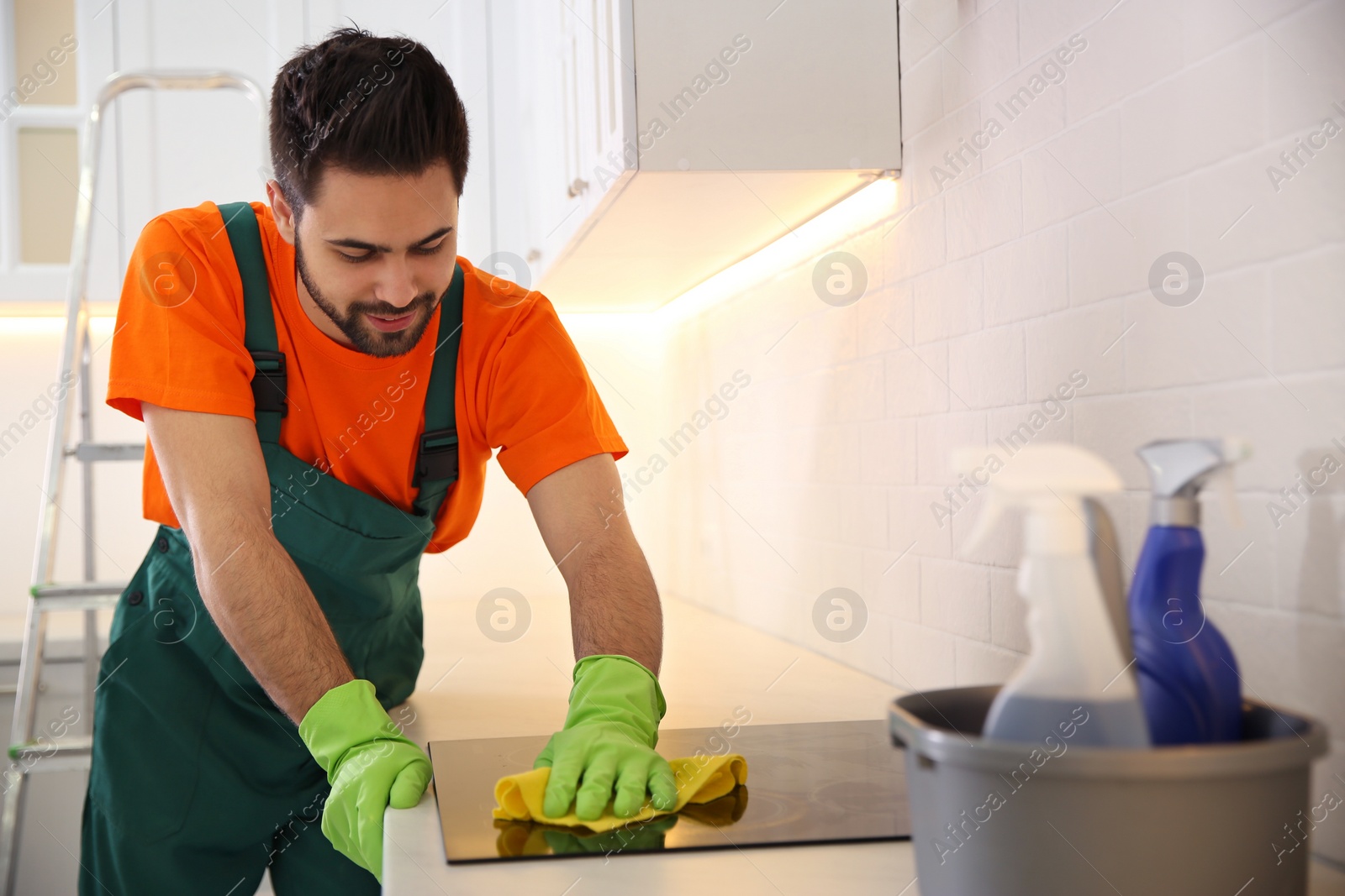 Photo of Professional young janitor cleaning stove in kitchen