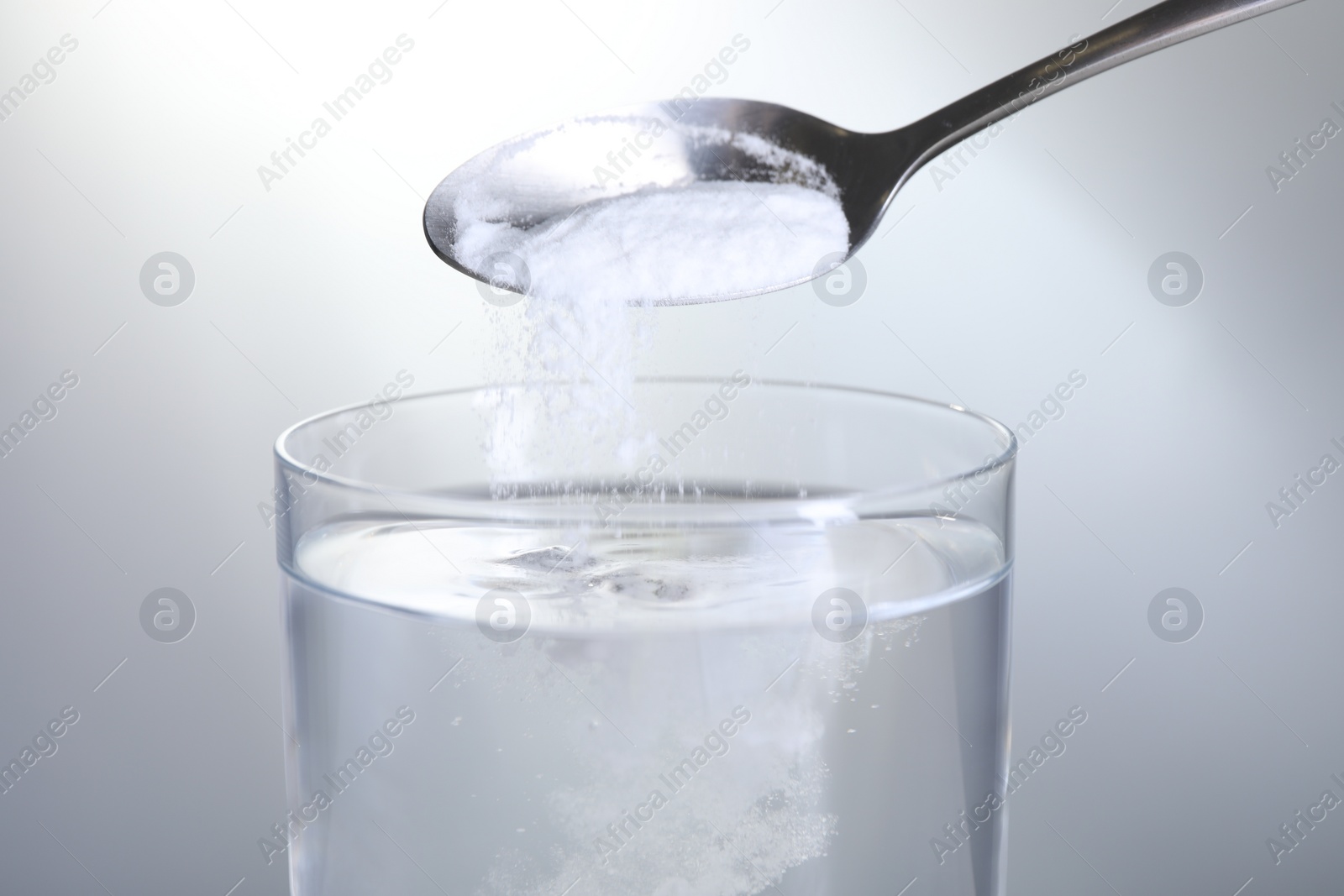 Photo of Adding baking soda into glass of water on light grey background, closeup