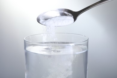 Photo of Adding baking soda into glass of water on light grey background, closeup