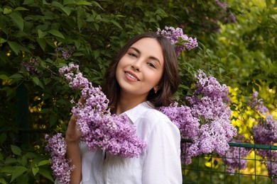 Attractive young woman near blooming lilac bush outdoors