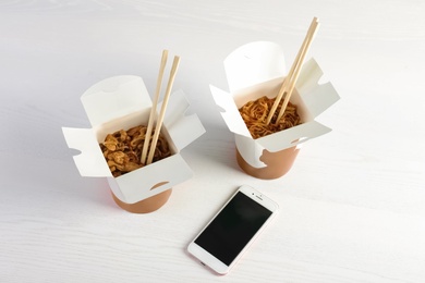 Photo of Mobile phone with space for text and Chinese noodles on white wooden table. Food delivery