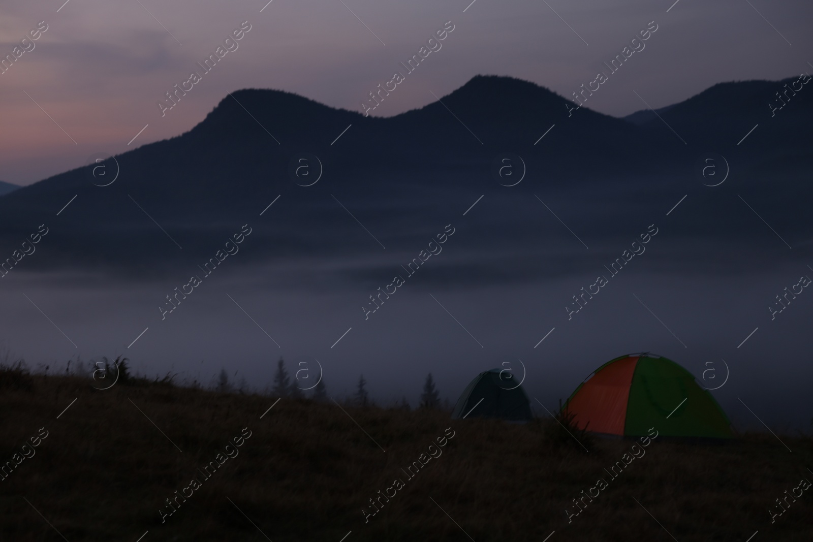 Photo of Picturesque view of mountain landscape with thick fog and camping tents at dawn