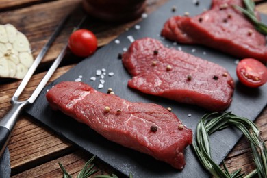 Photo of Fresh raw meat steaks and spices on wooden table, closeup