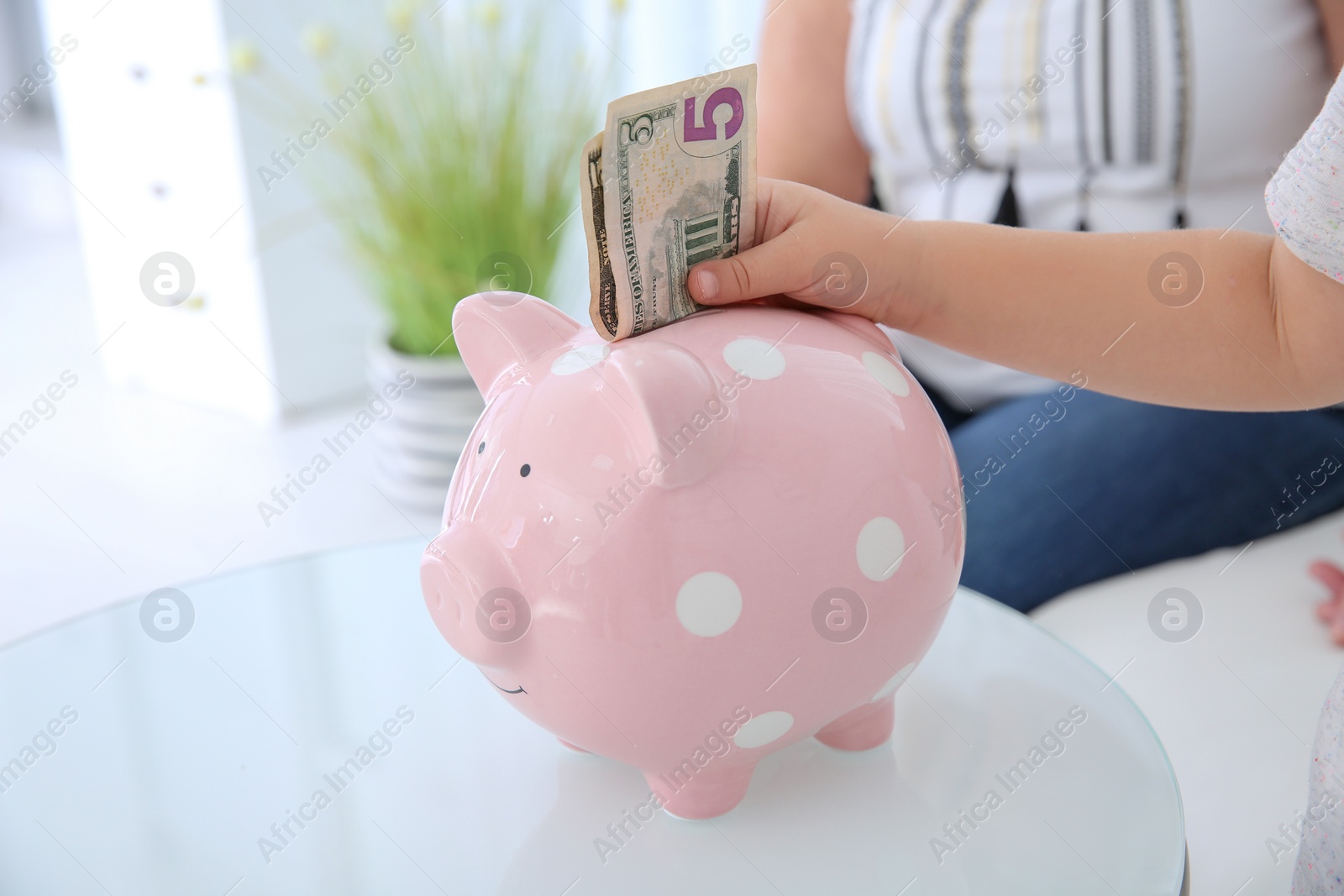 Photo of Little girl putting money into piggy bank at table, closeup