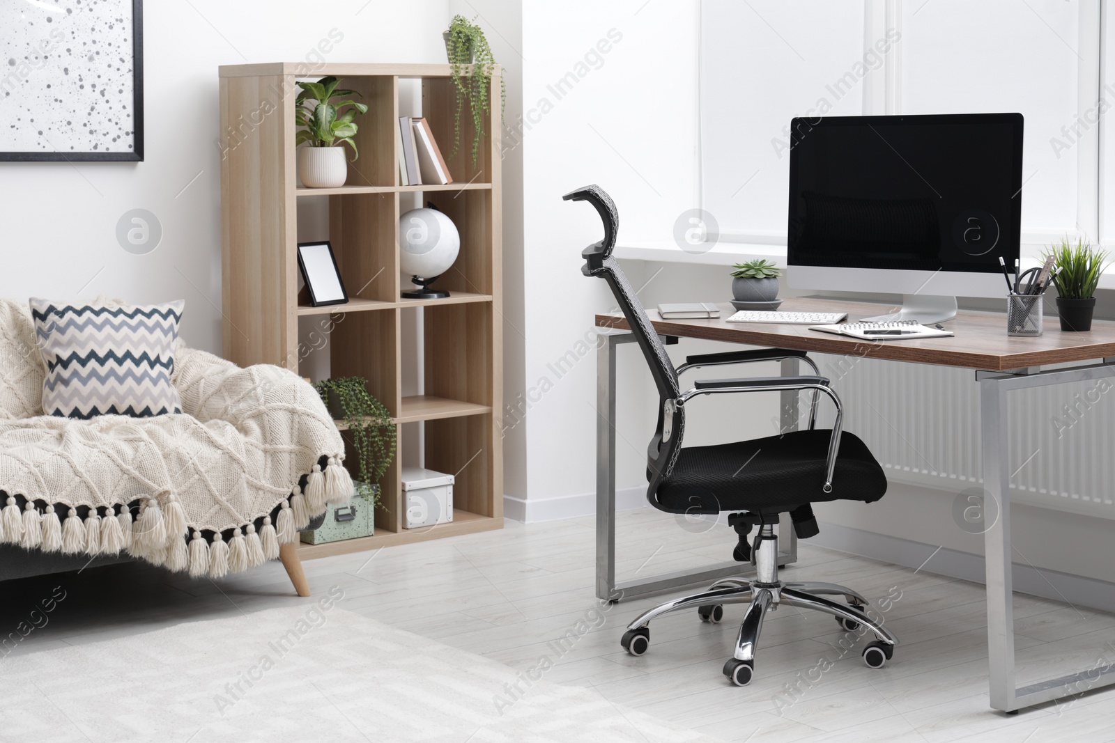 Photo of Cosy workspace with computer on desk, stylish furniture and potted plants at home