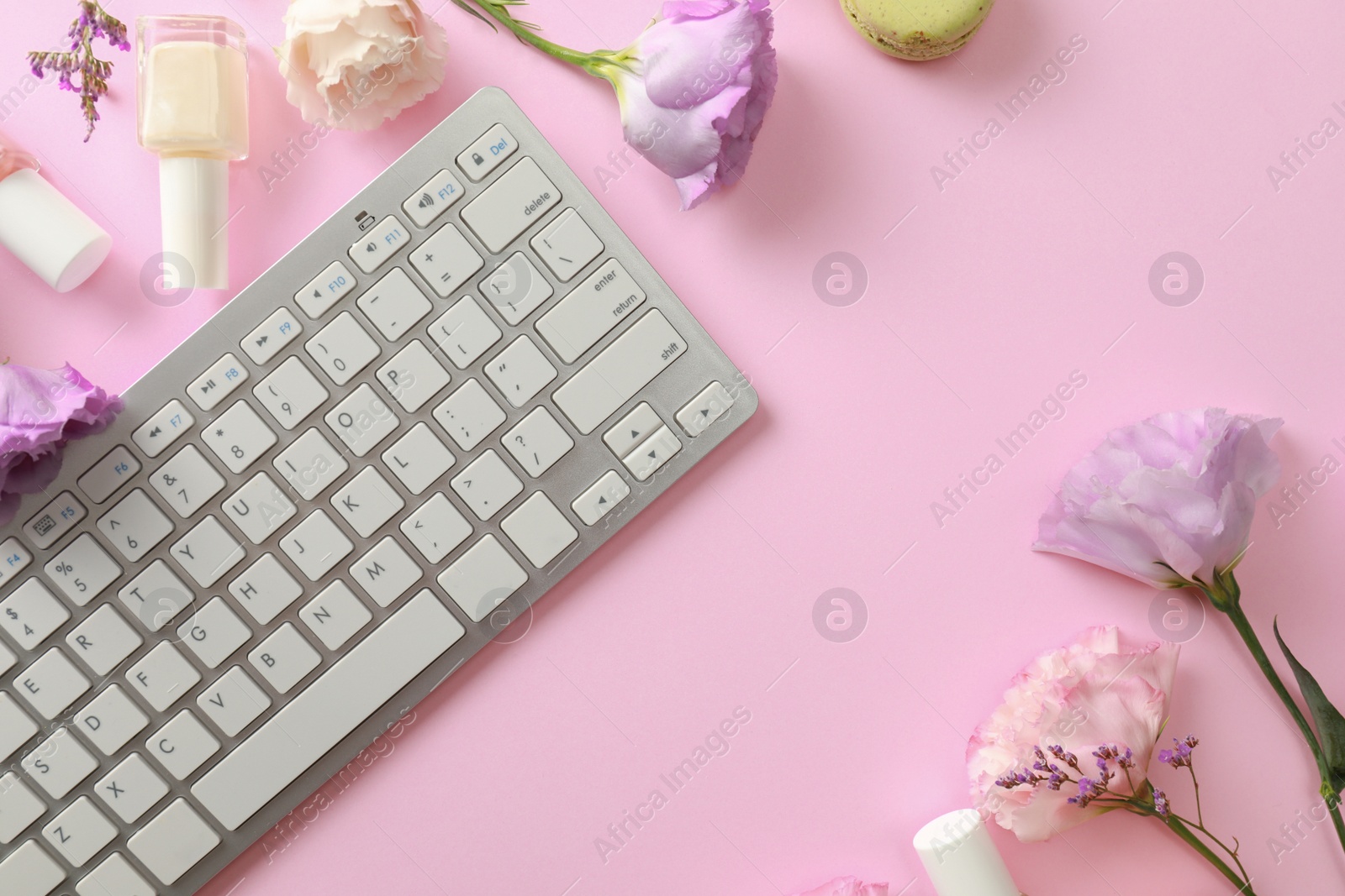 Photo of Flat lay composition with keyboard and flowers on pink background. Beauty blogger's workplace
