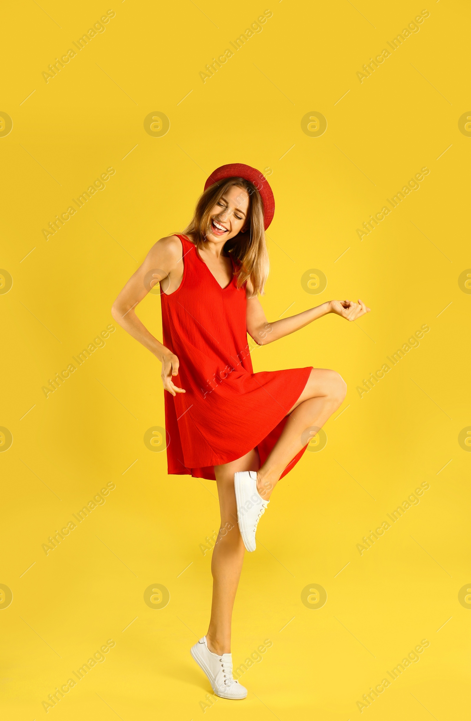 Photo of Beautiful young woman in red dress dancing on yellow background