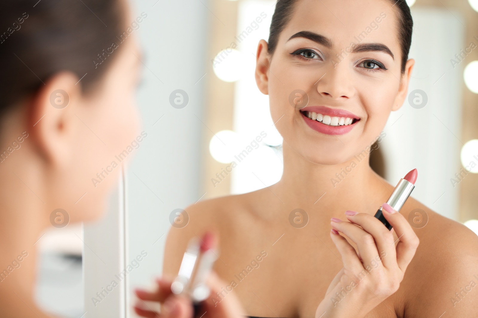 Photo of Young woman applying lipstick in front of mirror