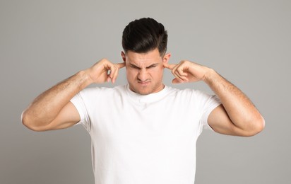 Photo of Emotional man covering ears with fingers on grey background