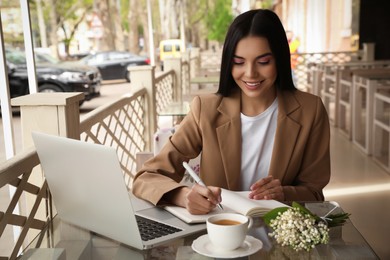 Photo of Woman with cup of coffee working at outdoor cafe in morning