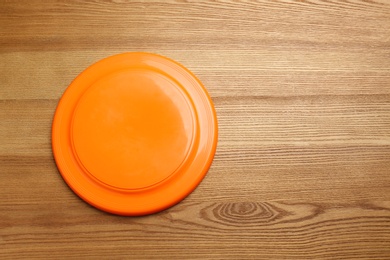 Photo of Orange plastic frisbee disk on wooden background, top view. Space for text