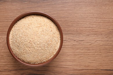 Fresh bread crumbs in bowl on wooden table, top view. Space for text
