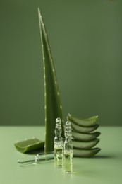 Skincare ampoules with extract of aloe vera and cut green leaves on color background