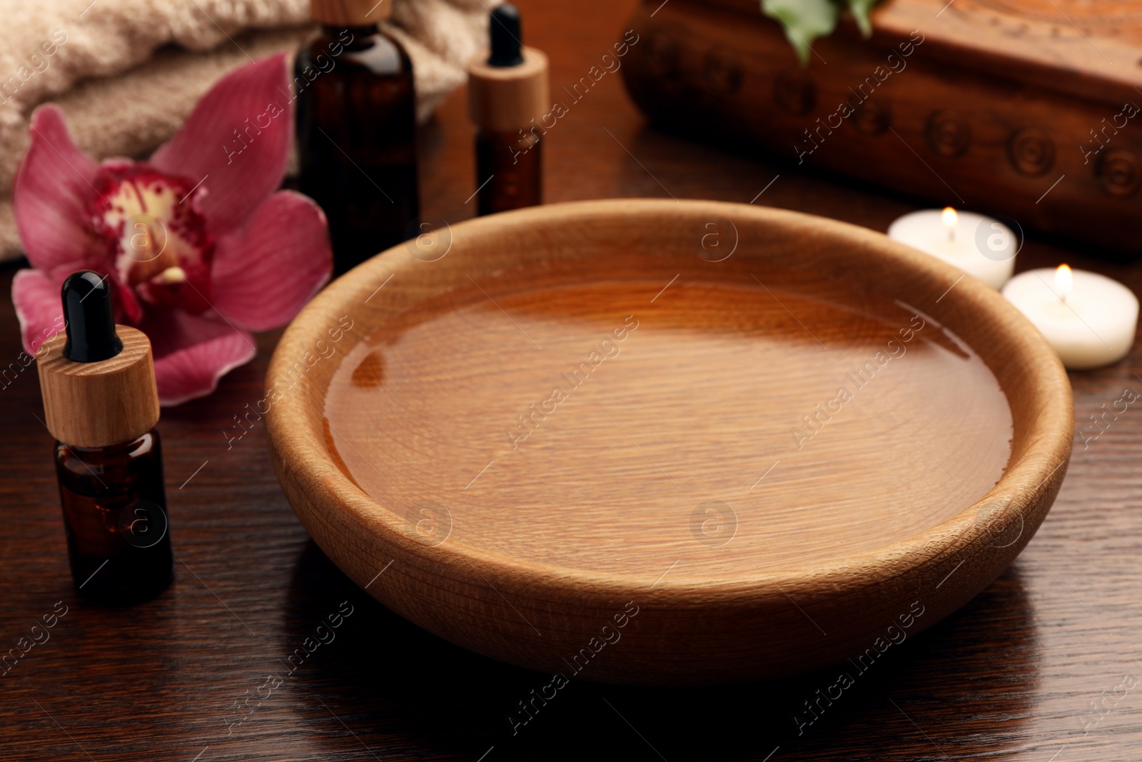 Photo of Bowl of water, bottles with essential oil and candles on wooden table. Aromatherapy treatment