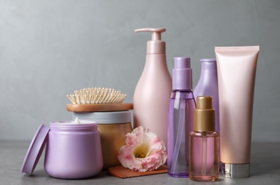 Different hair products, flower and brush on grey table