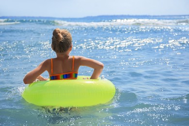 Beach holiday. Little girl with inflatable ring in sea on sunny day, back view. Space for text