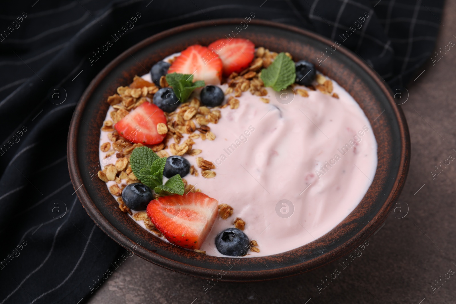 Photo of Bowl with yogurt, berries and granola on brown table