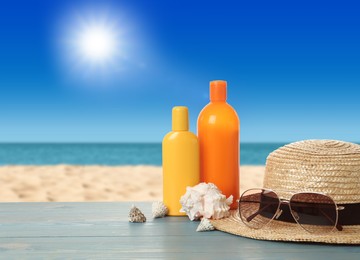 Image of Different bottles of skin sun protection body cream and beach accessories on light blue wooden table against seascape. Space for design