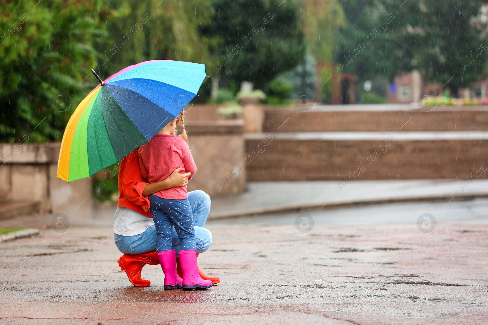 Photo of Mother and daughter with bright umbrella under rain outdoors