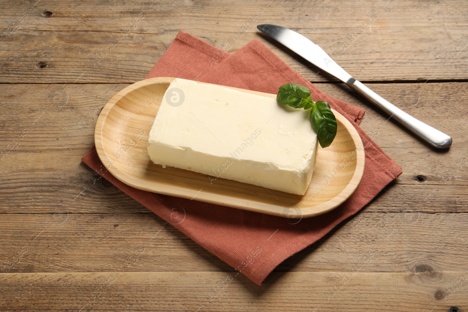 Photo of Block of tasty butter with basil and knife on wooden table