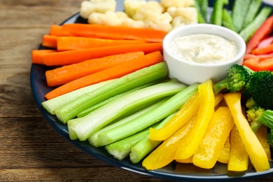 Photo of Plate with celery sticks, other vegetables and dip sauce on wooden table, closeup