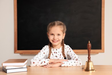 Photo of Pupil sitting at desk with school bell and books in classroom