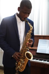 Photo of African-American man playing saxophone indoors. Talented musician