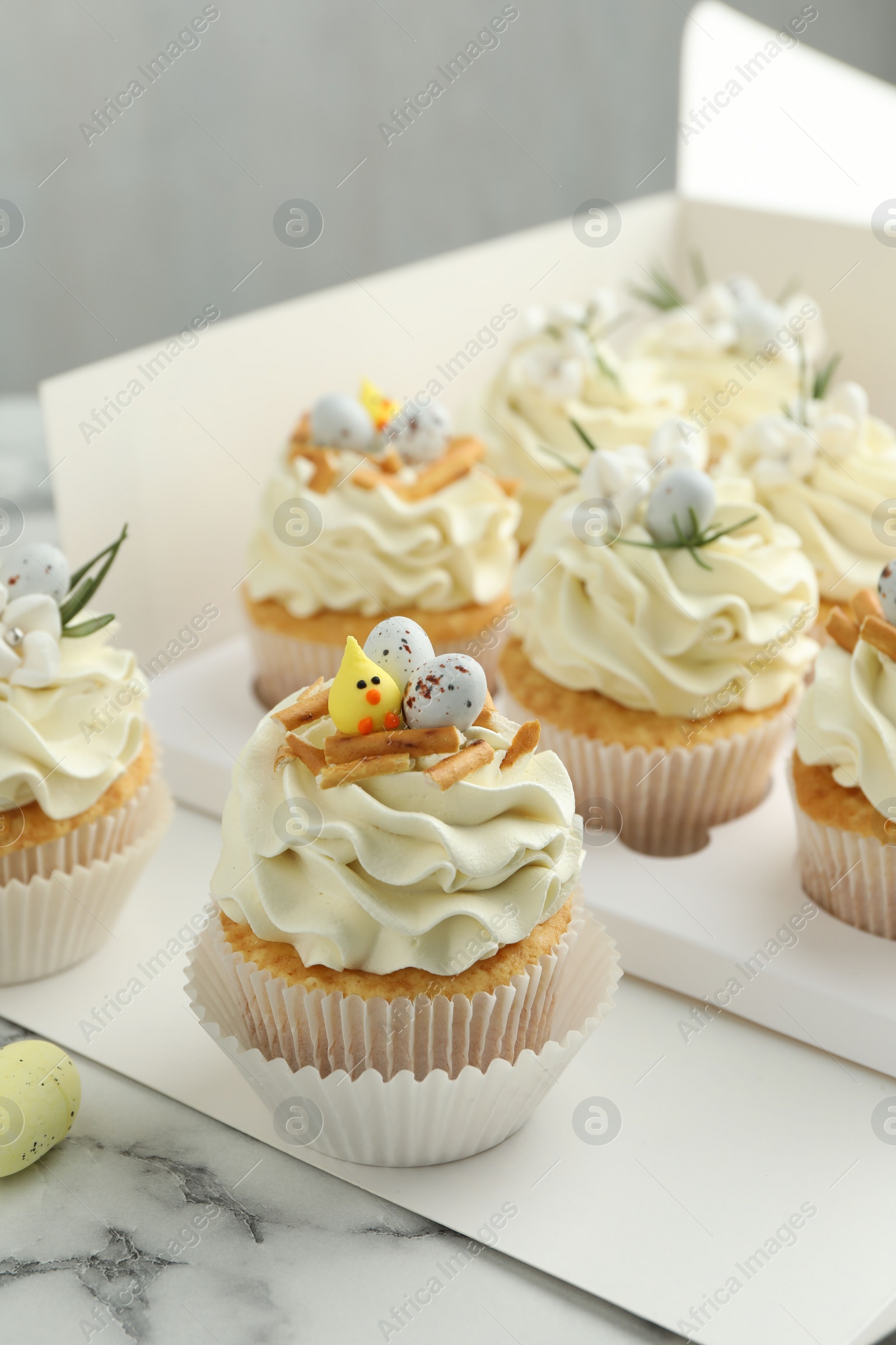 Photo of Tasty Easter cupcakes with vanilla cream on white marble table, closeup