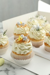 Photo of Tasty Easter cupcakes with vanilla cream on white marble table, closeup