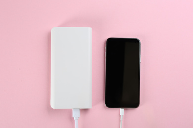 Mobile phone charging with power bank on pink background, flat lay