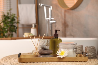 Different spa products and beautiful flower on wicker table in bathroom