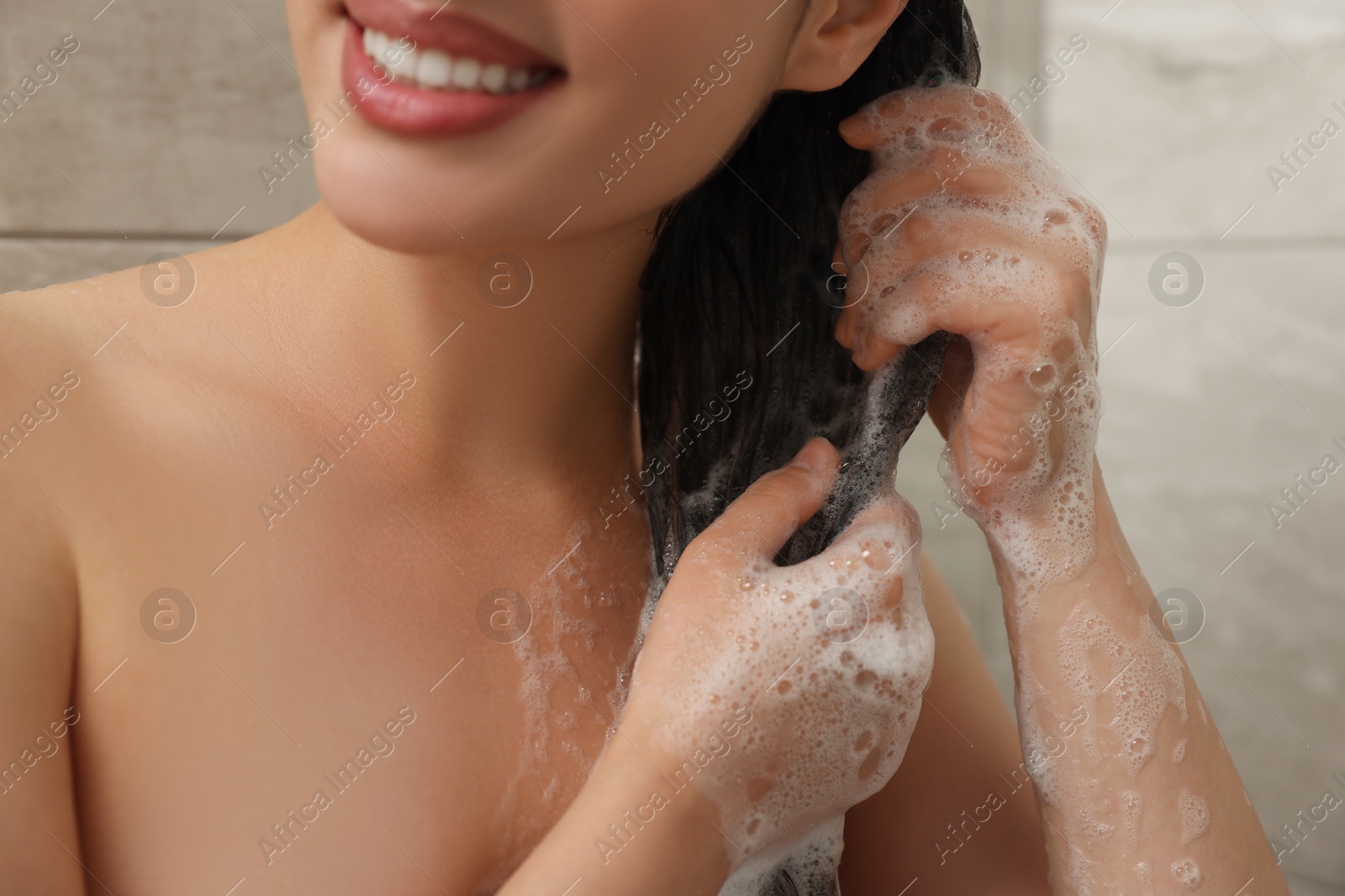 Photo of Happy woman washing hair with shampoo in shower, closeup