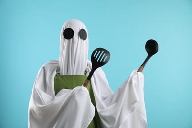 Woman in ghost costume and apron with kitchen set on light blue background