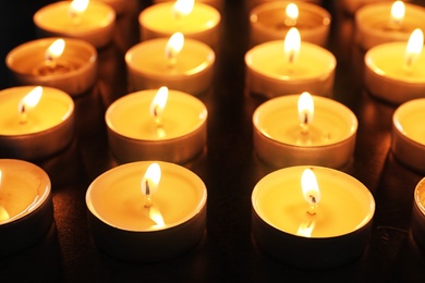 Wax candles burning on table in darkness, closeup