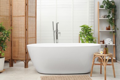 Photo of Spa day. Stylish bathroom interior with ceramic tub and green houseplants