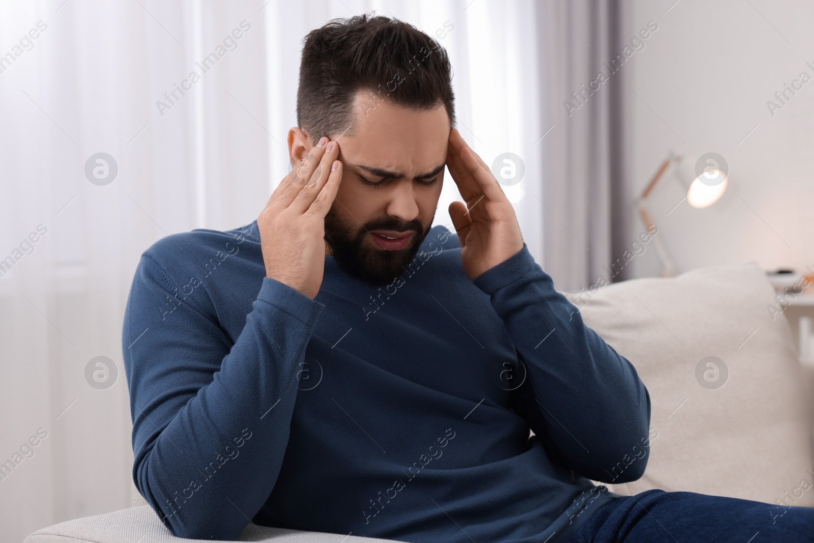 Photo of Man suffering from headache on sofa at home