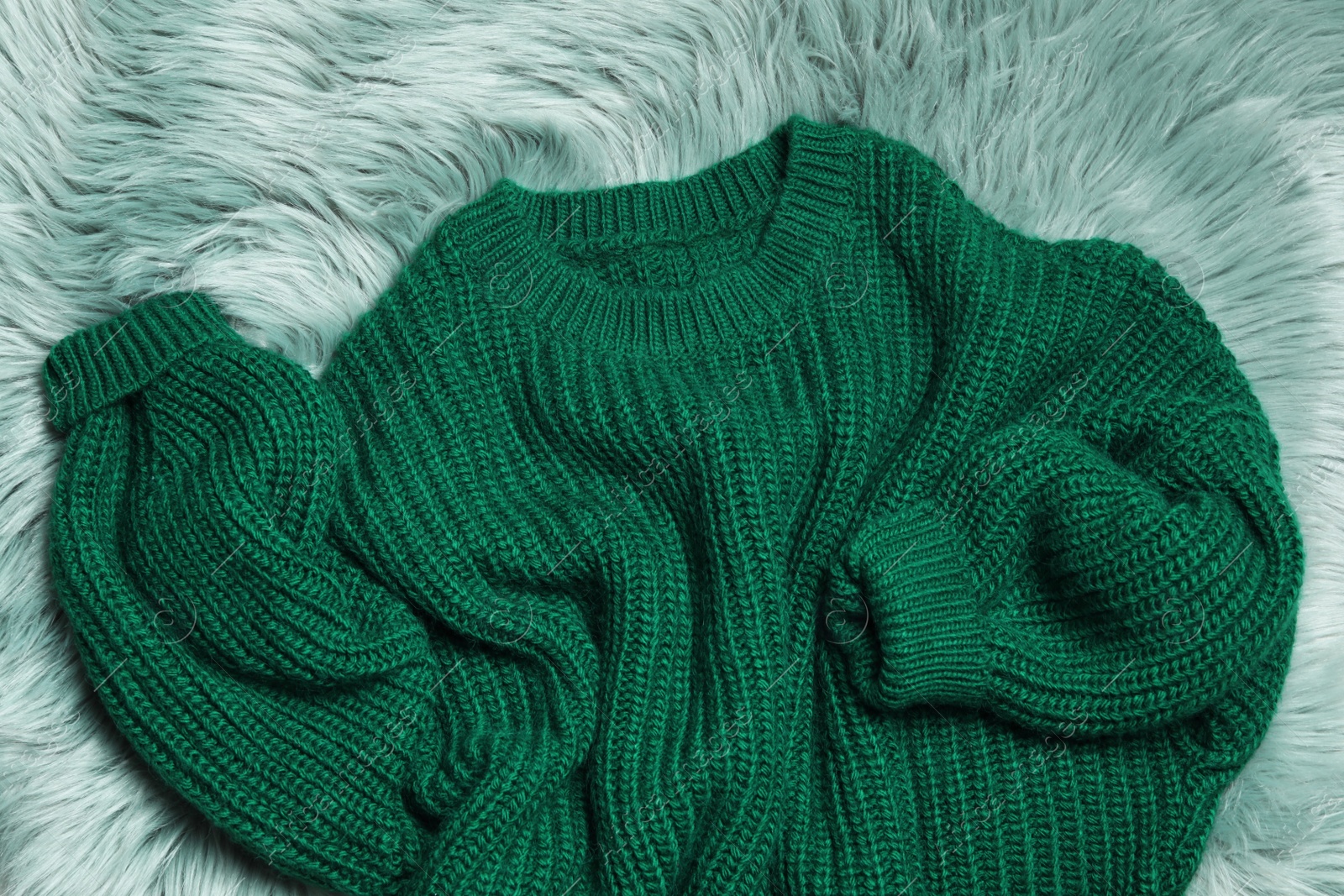 Photo of Soft knitted sweater on green fur rug, flat lay
