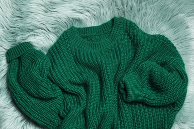 Soft knitted sweater on green fur rug, flat lay
