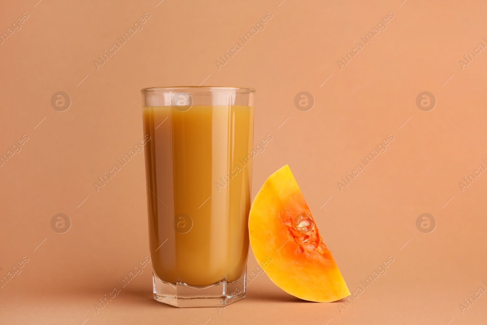 Photo of Tasty pumpkin juice in glass and cut pumpkin on pale orange background