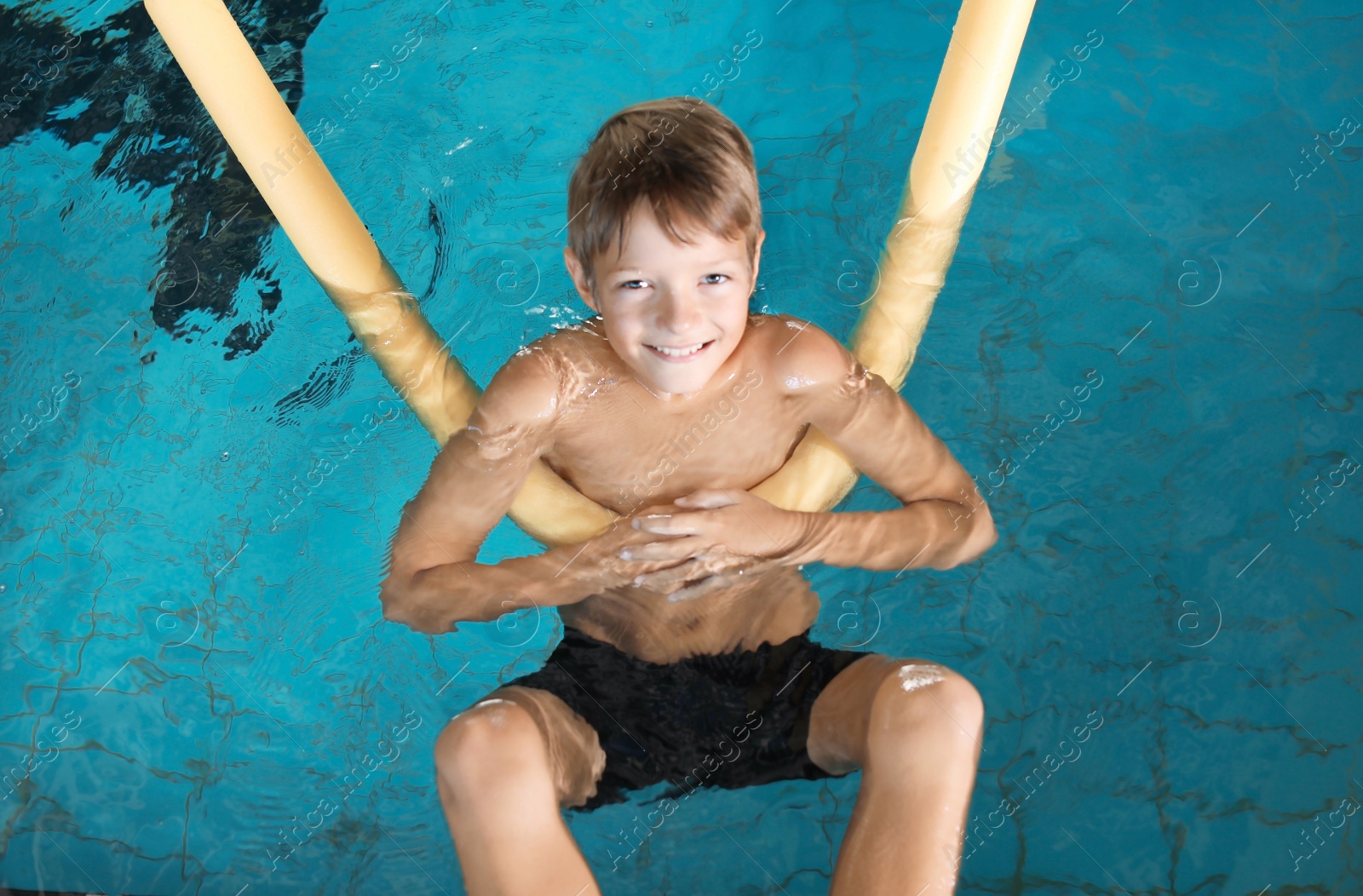 Photo of Little boy with swimming noodle in indoor pool