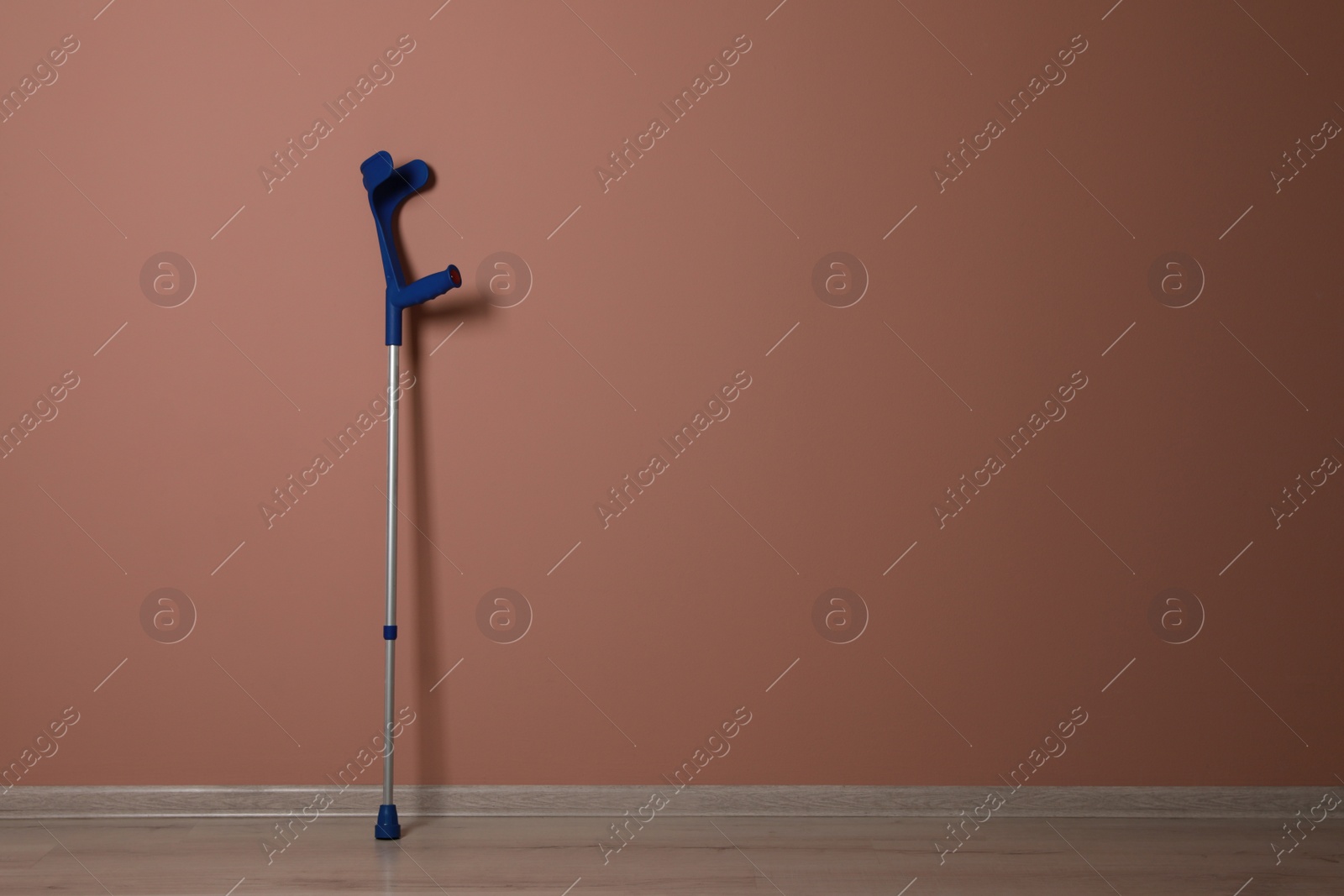 Photo of Elbow crutch near pale pink wall. Space for text