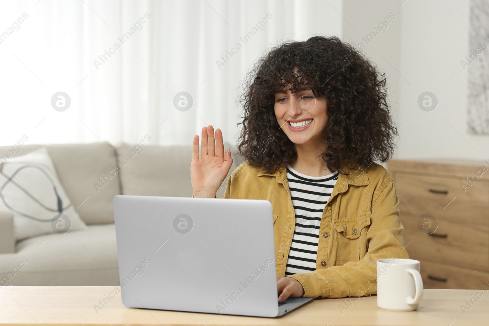 Photo of Happy woman waving hello during video call at table in room